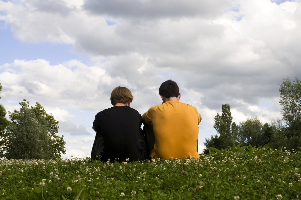twee jongeren zitten in het gras met de rug naar de kijker toe - mentaal welzijn jongeren verslechtert
