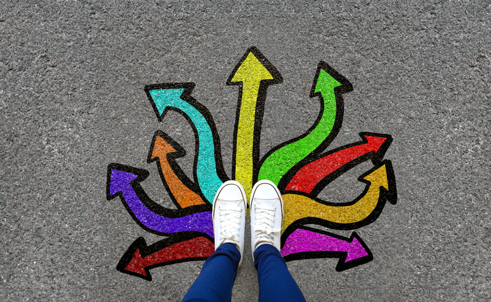 Feet and arrows on road background. Pair of foot standing on tarmac road with colorful graffiti arrow sign choices, creative and idea concept. Selfie woman wearing white shoe or sneaker. Top view. *** Local Caption *** © Mananya Kaewthawee / Getty Images / iStock